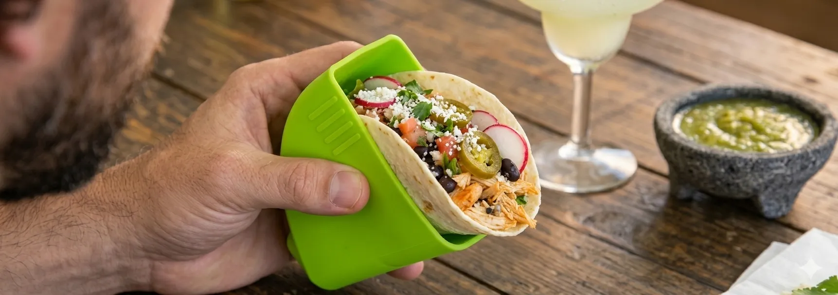Green Taco Grip keeps hands off your taco A hand holding a green Taco Grip around a filled taco, keeping fingers off the tortilla.